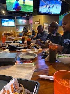 People eating at a Hooters restaurant, watching sports on multiple TVs. Food and drinks are on the table.