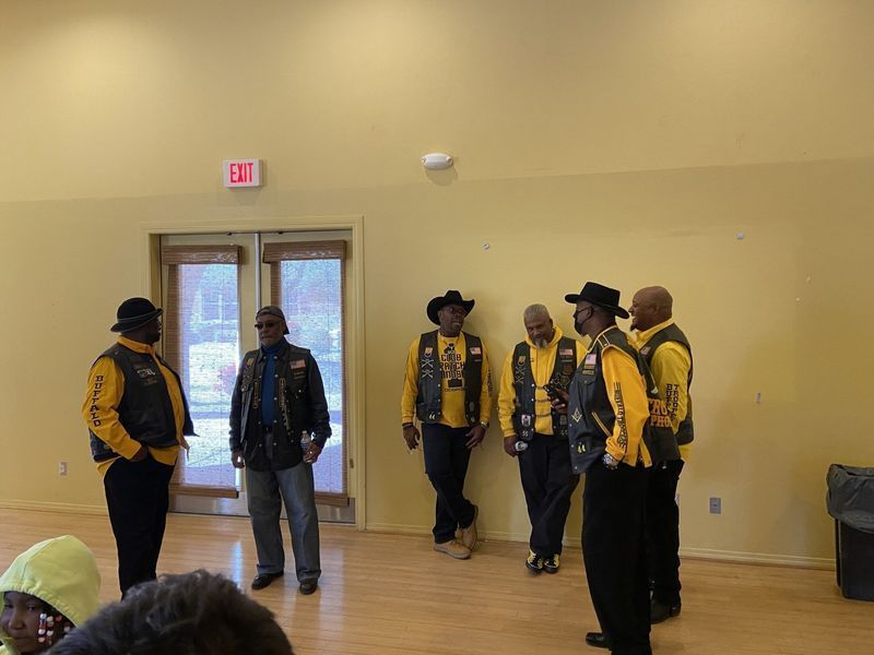 Group of people in black and yellow vests indoors, standing near a doorway.