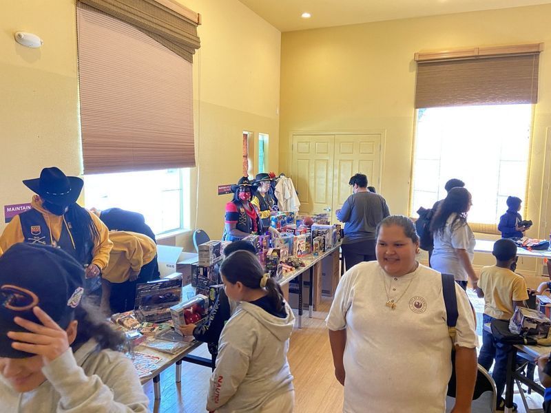 People browse merchandise at an indoor event, light-filled room with tables, windows, and vendors.