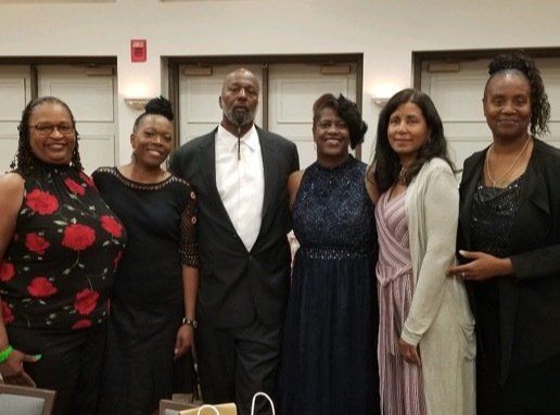 Group of six people, formally dressed, posing indoors.