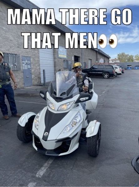 Man riding a white three-wheeled motorcycle in a parking lot. Two bystanders watch. The text reads: 