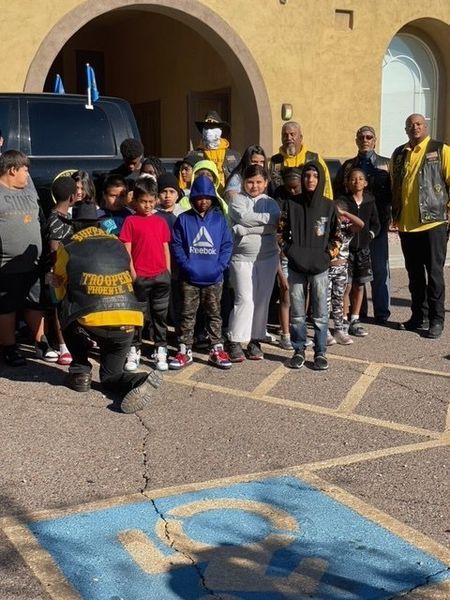 Group of children with adults in front of a building. One adult kneels near a disabled parking space.