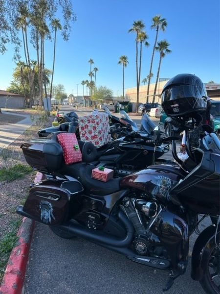 Motorcycle with gifts strapped on, parked on the street with palm trees in the background.