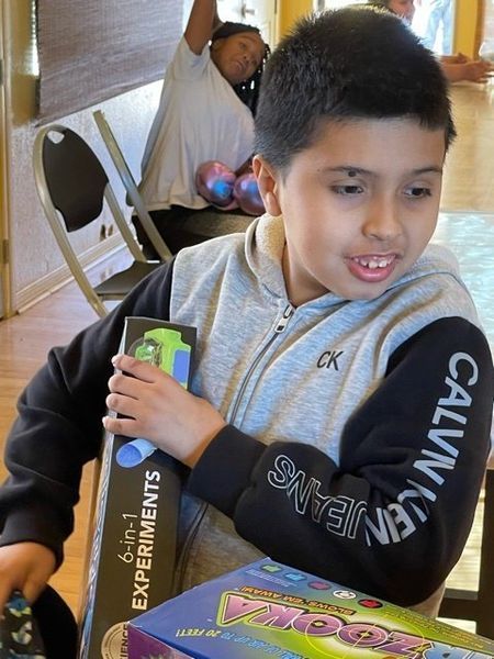 Boy holding a science experiment box, smiling, wearing a Calvin Klein hoodie.