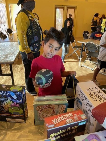 Boy holding football and bag, surrounded by games, with others in a room.