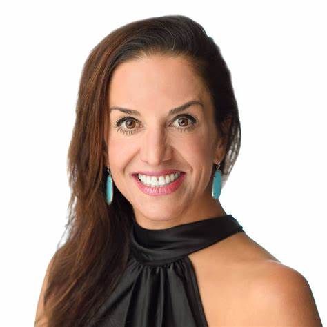 A woman wearing a black top and earrings is smiling for the camera.