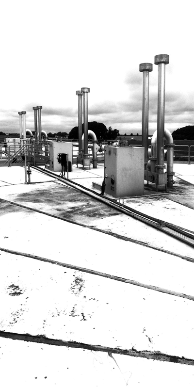 A black and white photo of a rooftop with pipes and chimneys.
