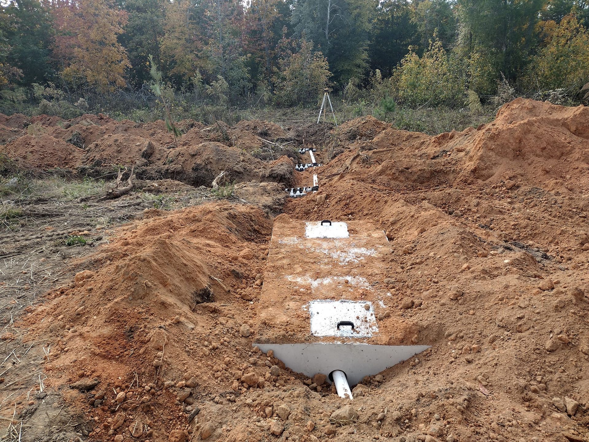 Excavated ground with installed septic system components; a field with trees in the background.