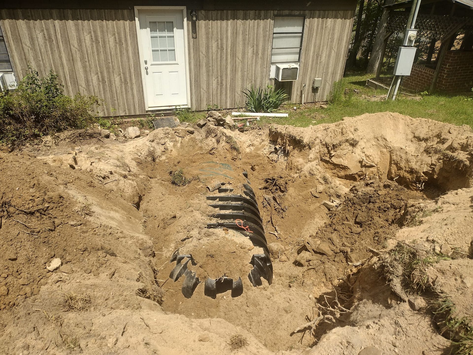 A trench dug in the ground with a black septic tank visible in front of a wooden building.