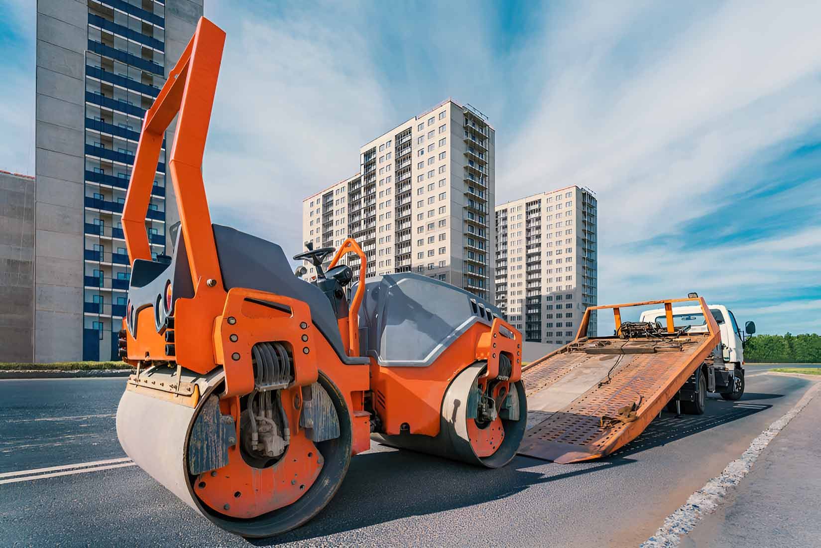 An Orange Road Roller Is Parked On The Side Of The Road Next To A Tow Truck — Gympie/Childers Towing Pty Ltd in Brisbane, QLD