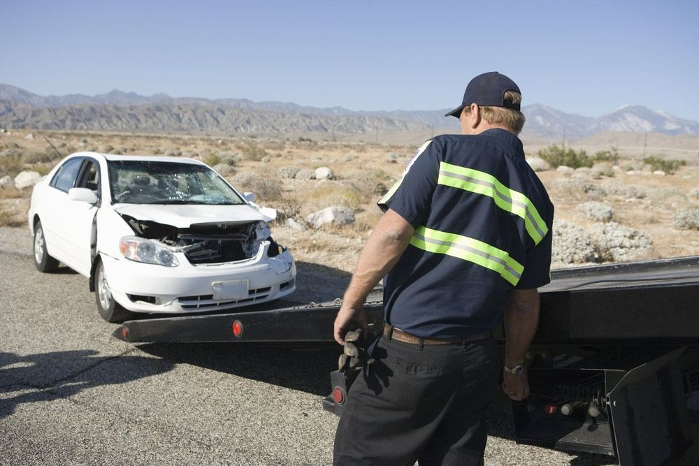 A Man Is Standing Next To A Tow Truck With A White Car On It — Gympie/Childers Towing Pty Ltd in Kingaroy, QLD