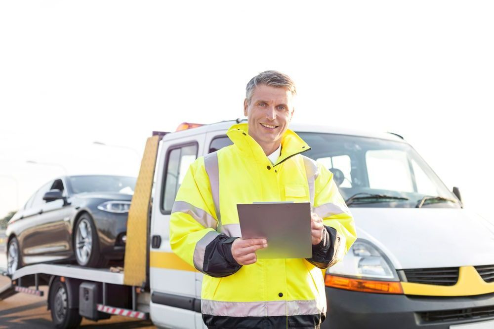 A Man Is Standing In Front Of A Tow Truck Holding A Tablet — Gympie/Childers Towing Pty Ltd in Kingaroy, QLD