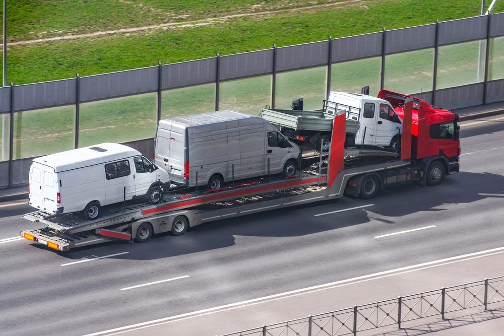 A Truck Is Carrying Two Vans On A Trailer On A Highway — Gympie/Childers Towing Pty Ltd in Maryborough, QLD