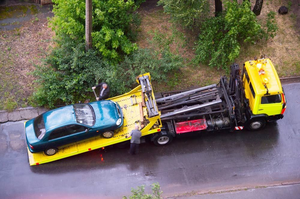 A Green Car Is Being Towed By A Yellow Tow Truck — Gympie/Childers Towing Pty Ltd in Gympie, QLD