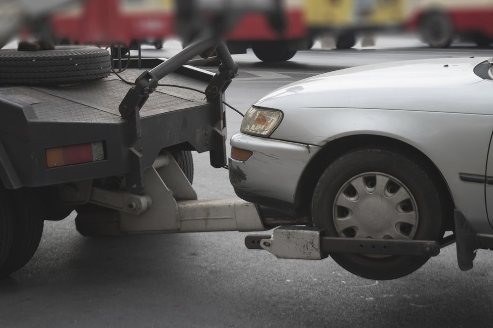 A White Car Is Being Towed By A Tow Truck — Gympie/Childers Towing Pty Ltd in Bundaberg, QLD