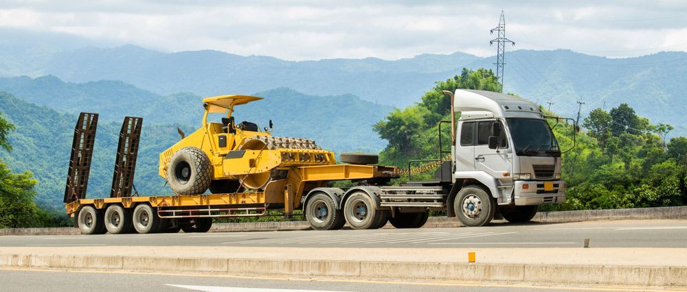A Truck Is Carrying A Yellow Bulldozer On A Trailer On A Highway — Gympie/Childers Towing Pty Ltd in Sunshine Coast, QLD