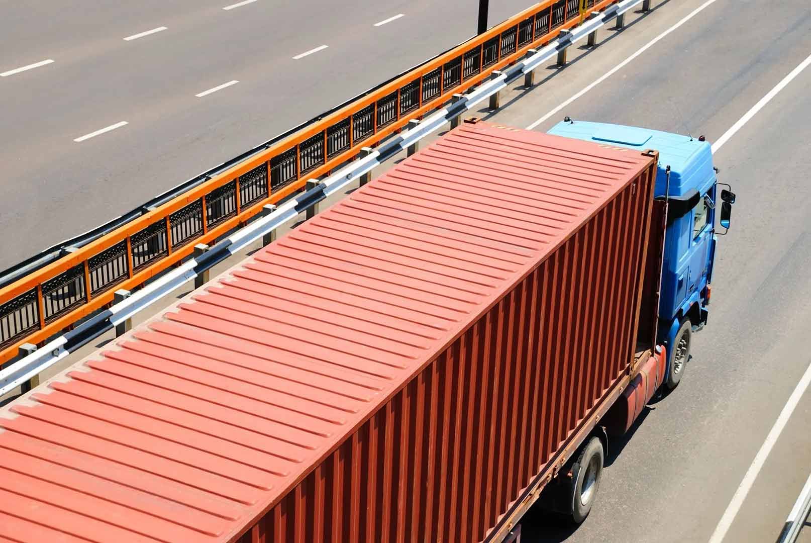 A Red Container Truck Is Driving Down A Highway — Gympie/Childers Towing Pty Ltd in Sunshine Coast, QLD
