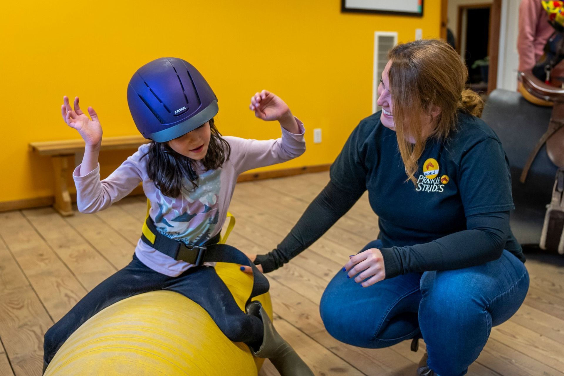 A woman is helping a young girl ride a yellow balance peanut.