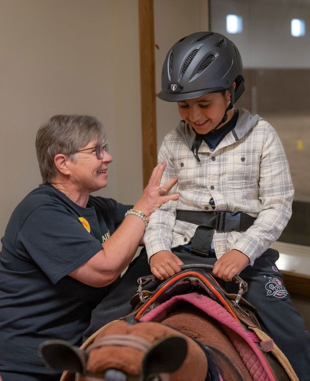 A volunteer is helping a young child on an exercise horse