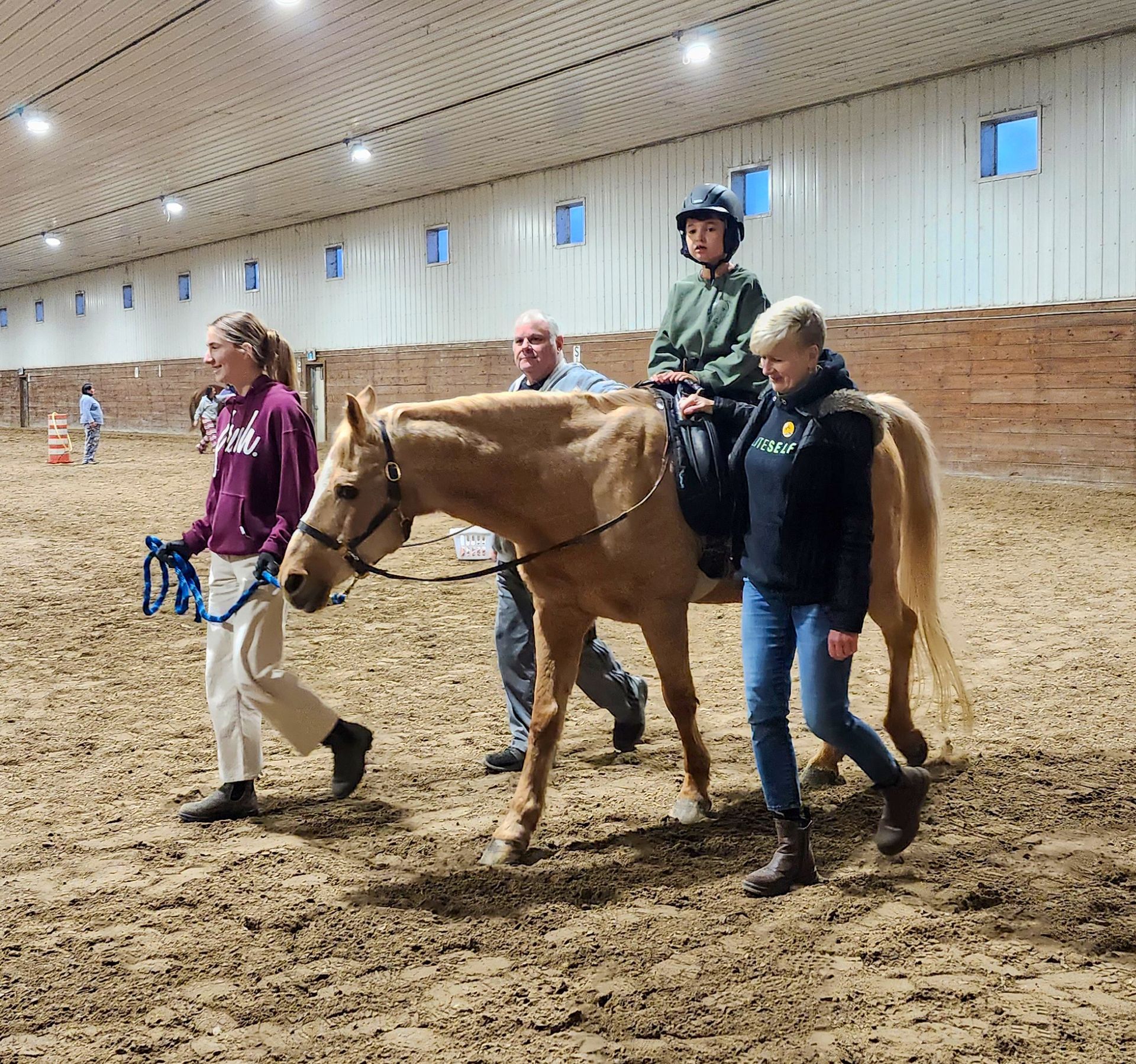 Child on a horse assisted by two people and a leader in an Indoor arena.