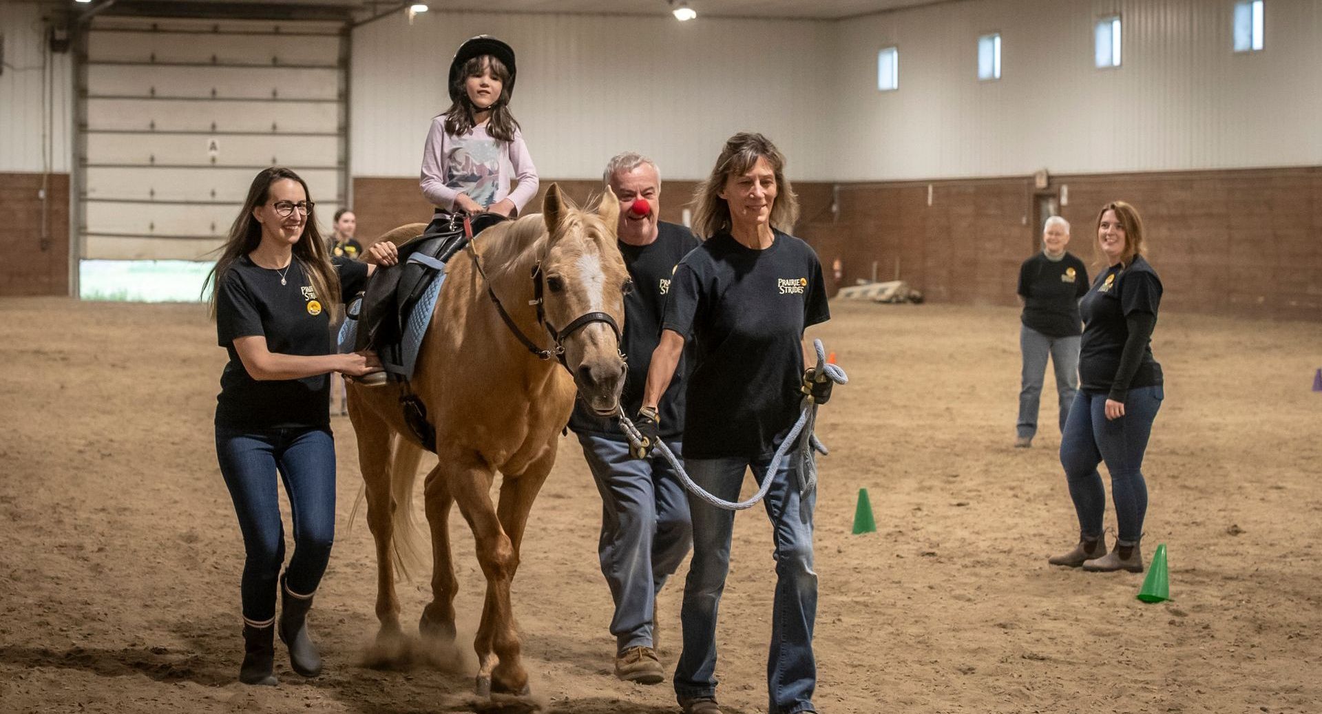 A little girl is riding a horse in an indoor arena with her sidewalkers and leader