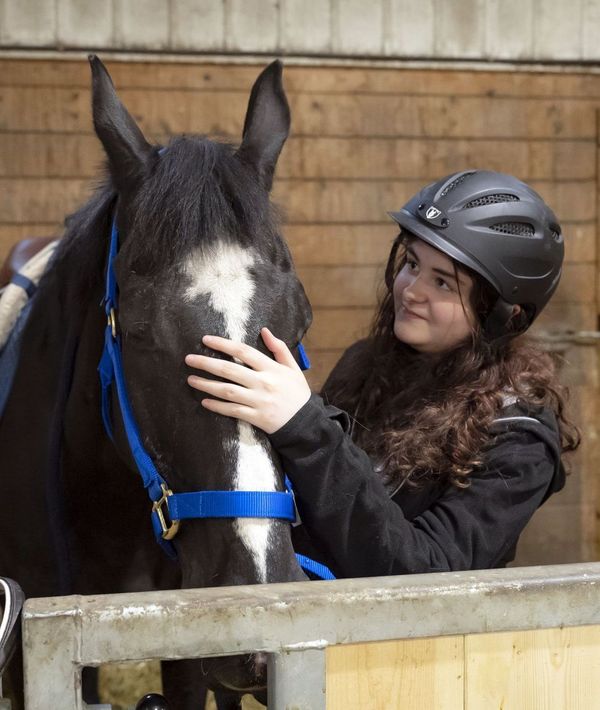 A teenage girl wearing a helmet is petting a black and white horse