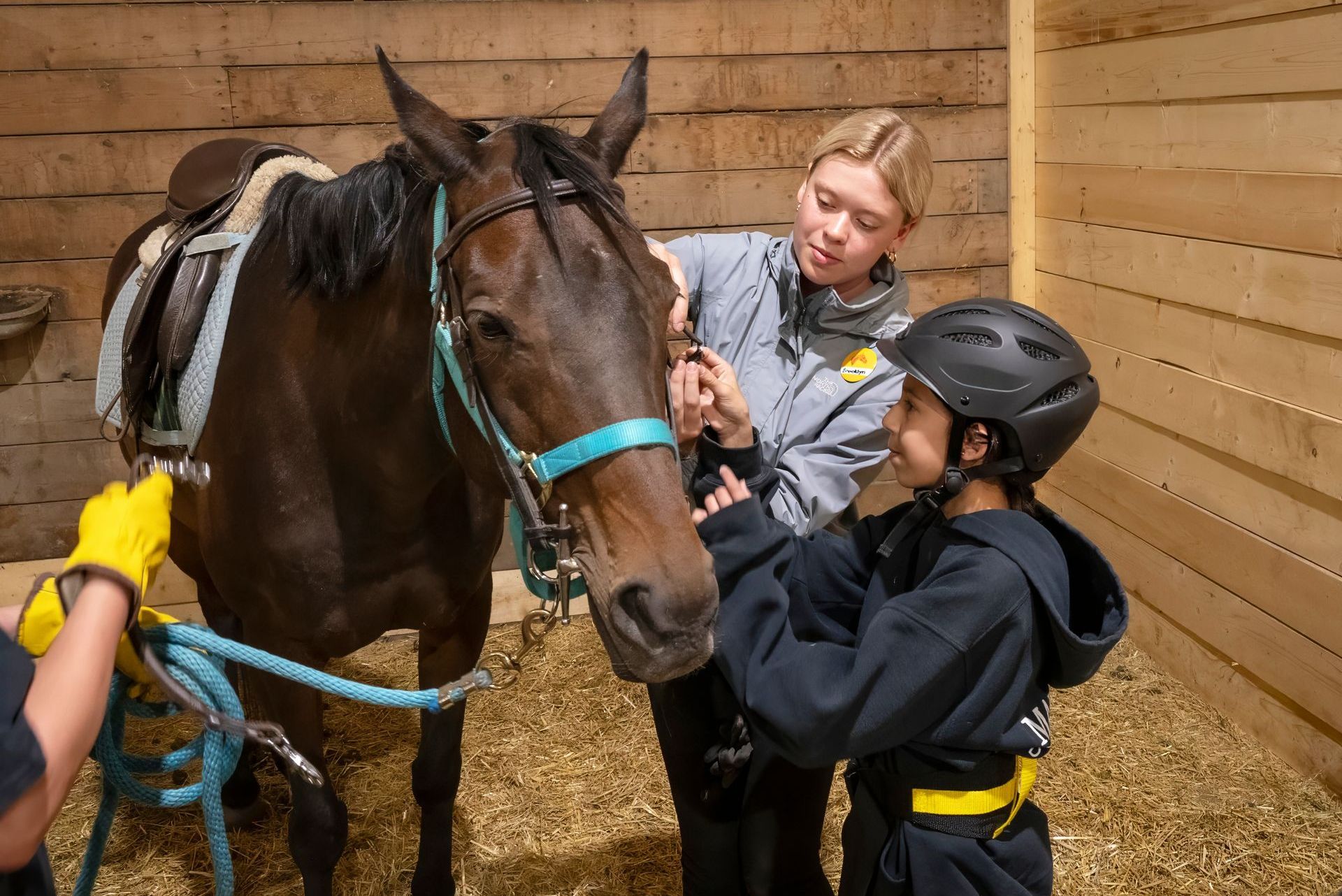 A woman and child are standing next to a horse in a stable.