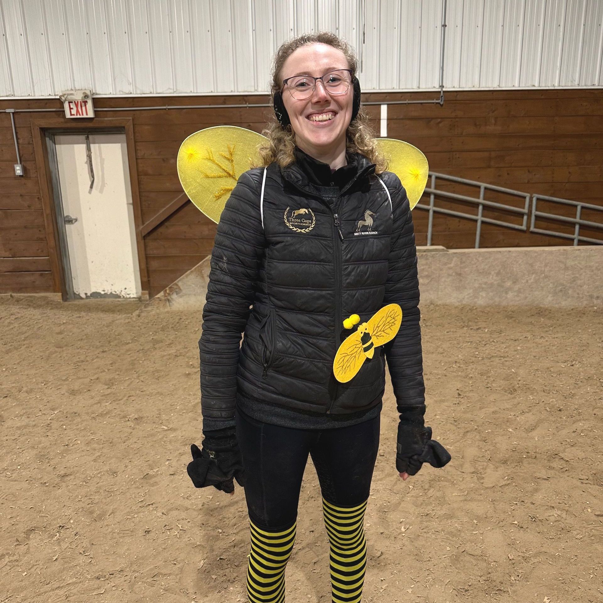 A woman in a black jacket and yellow bee wings and socks is smiling