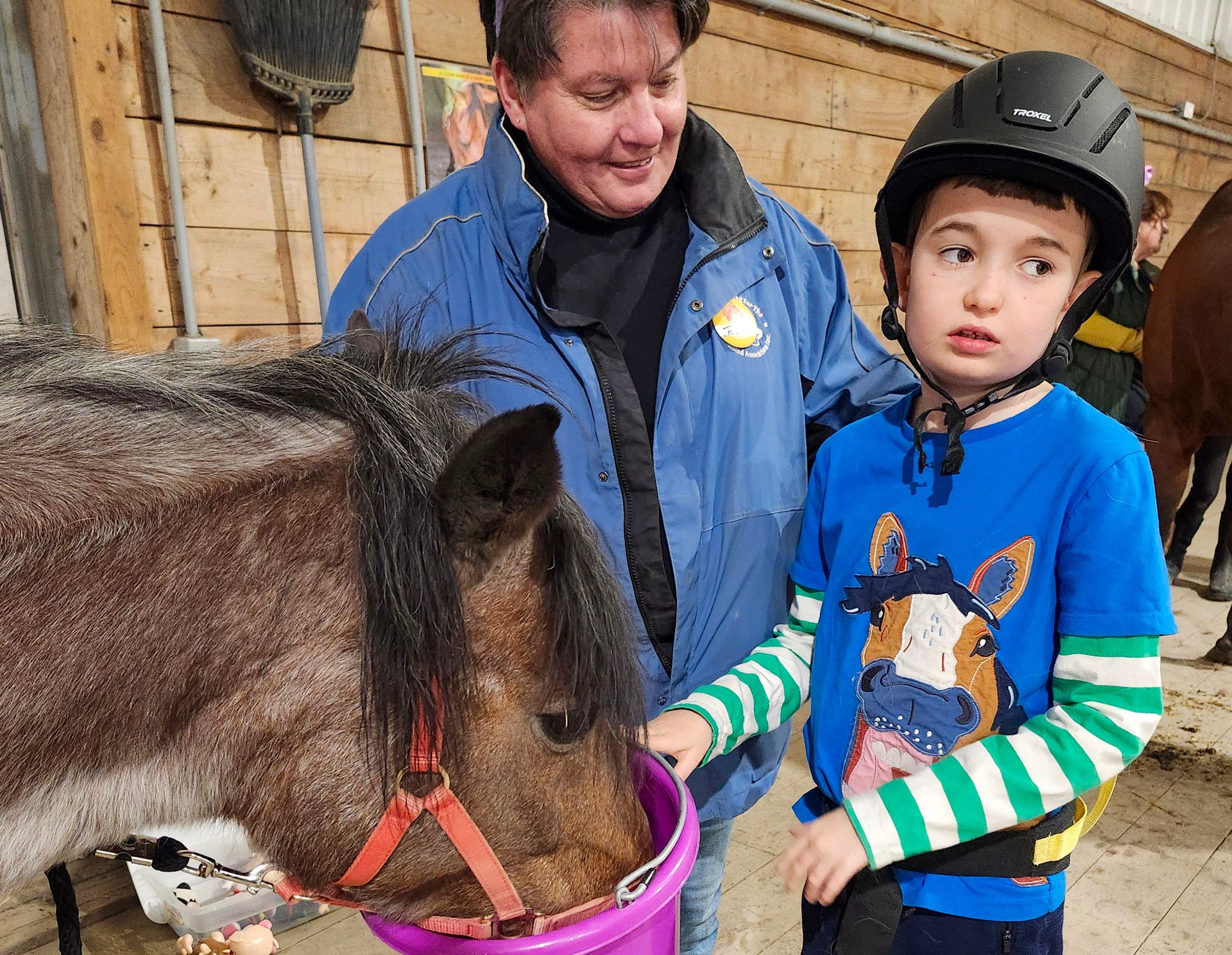 A woman and a young boy feed a horse in a stable. 