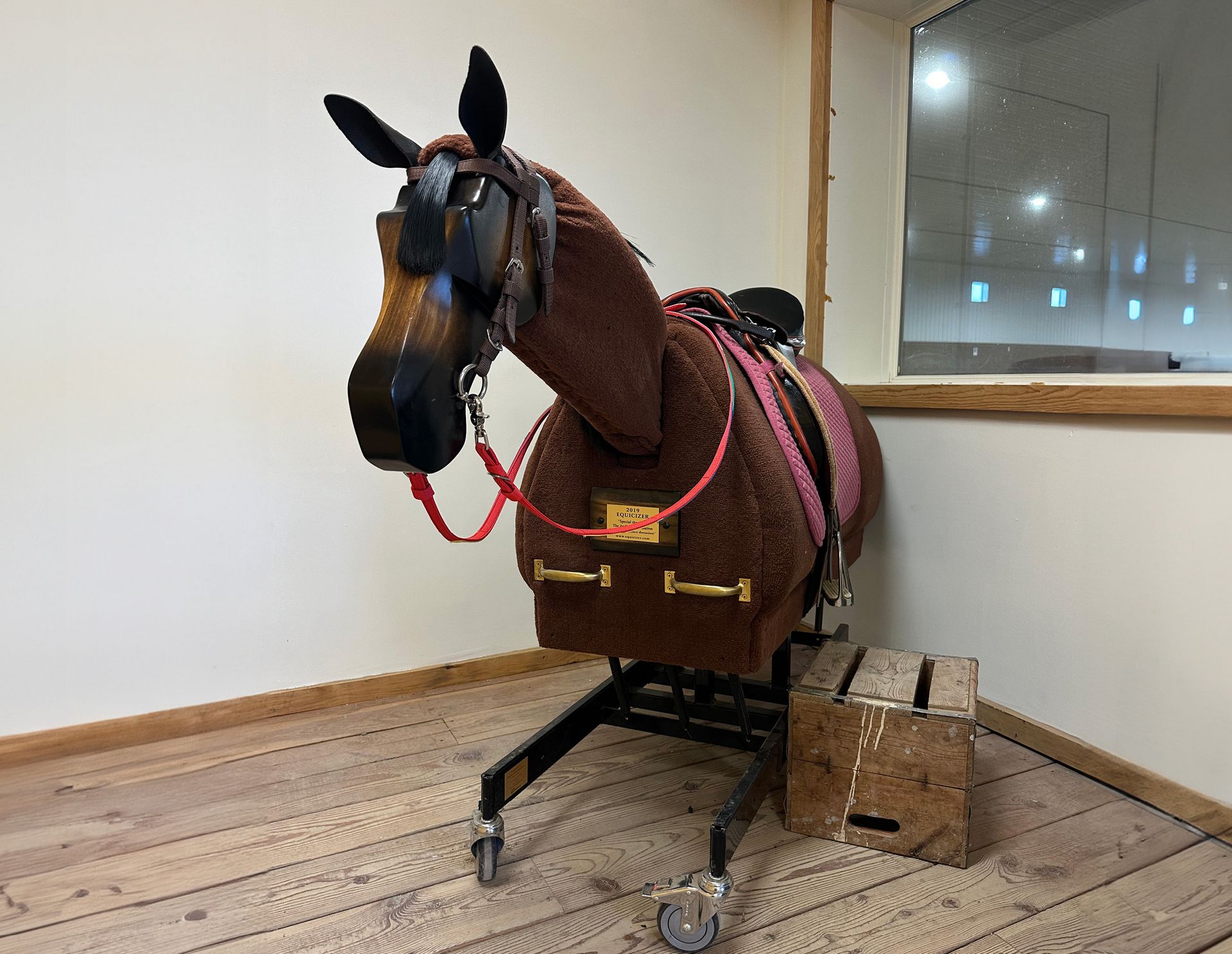 Brown mechanical horse with saddle, set on wheels, indoors.