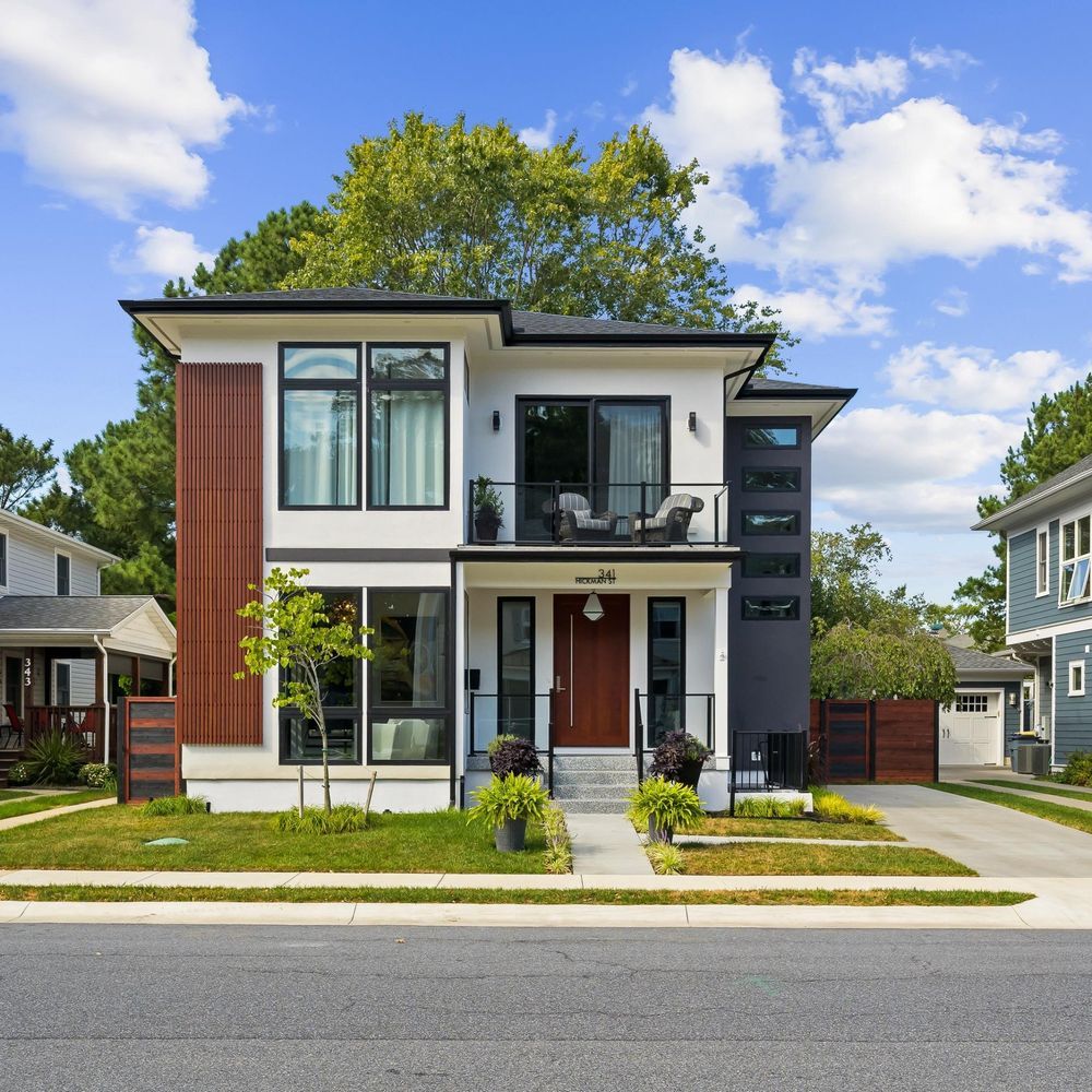 Modern two-story house with white and brown facade, black trim, small balcony, front yard, and concrete walkway.