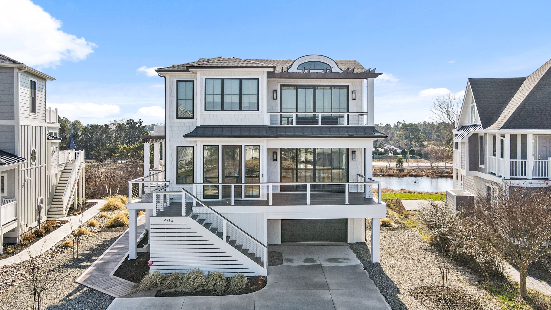 Modern white beach house with large windows, deck, and driveway.