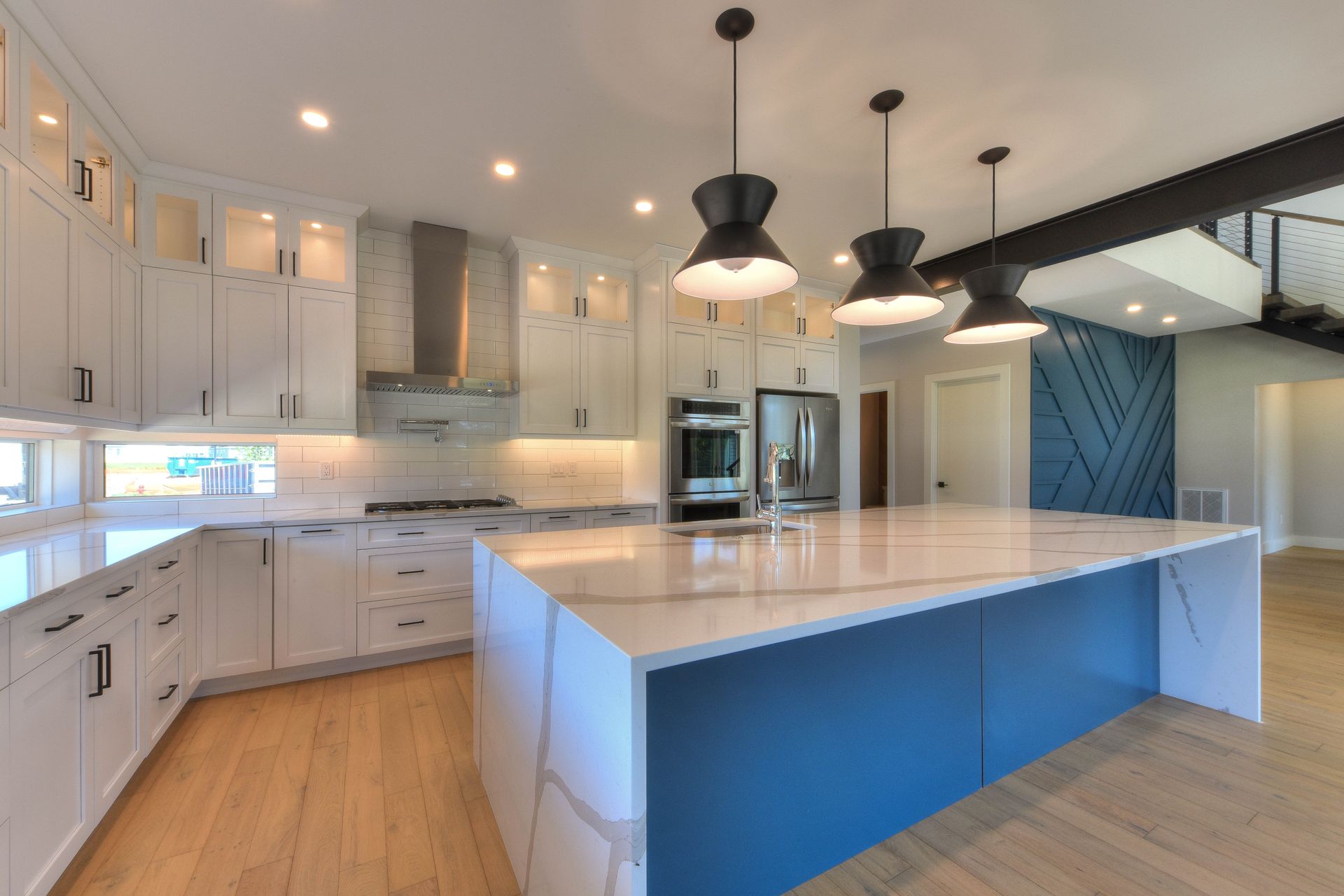 Bright modern kitchen with white cabinets, blue island, and black pendant lights.