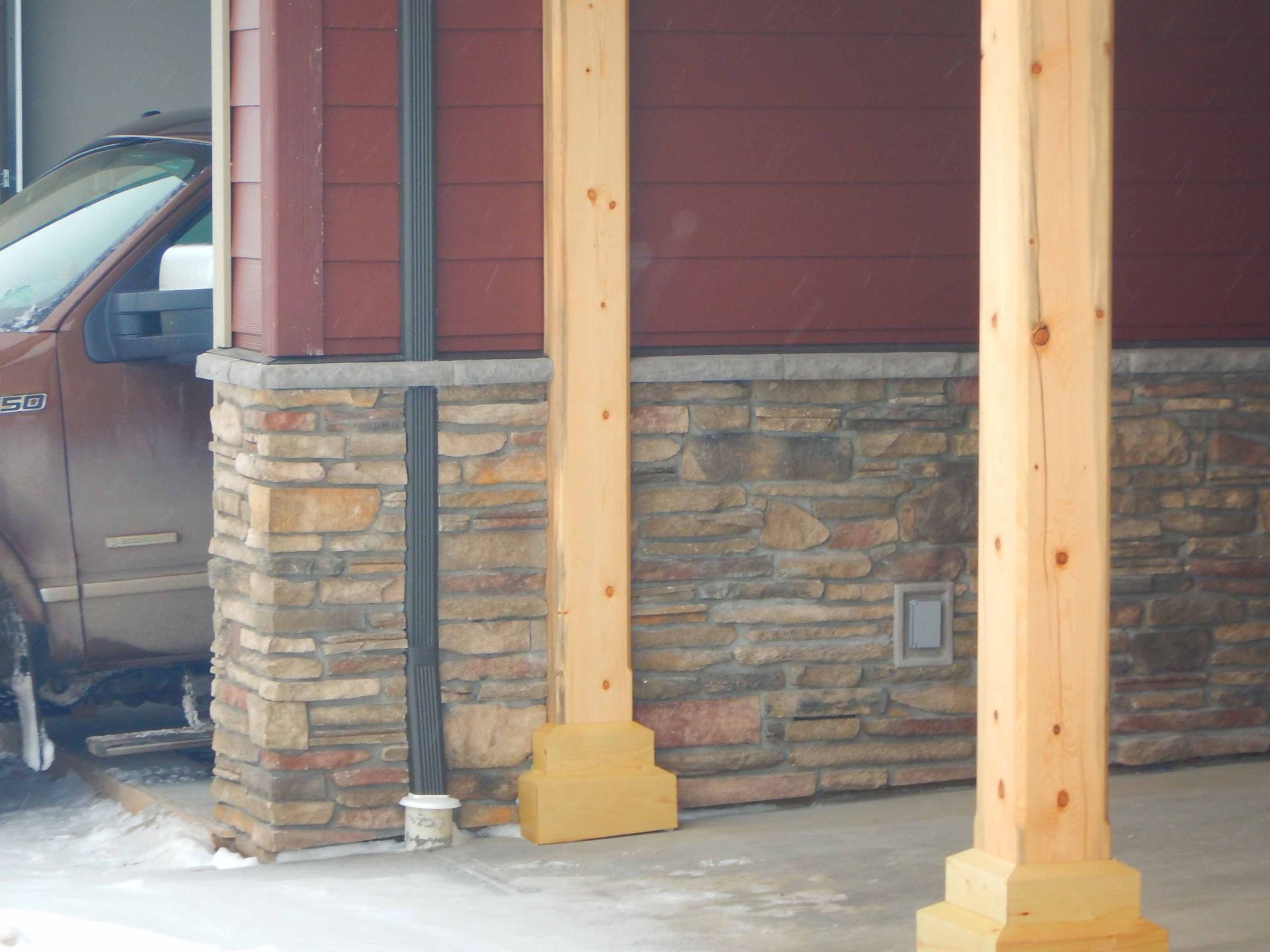 A car is parked under a wooden pillar in front of a stone wall