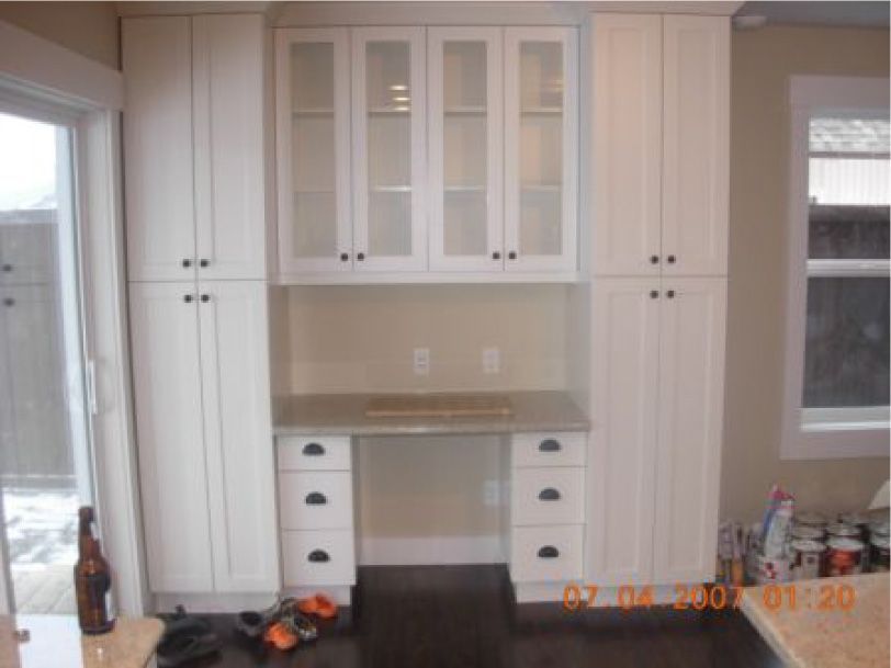 A kitchen with white cabinets and a desk with glass doors