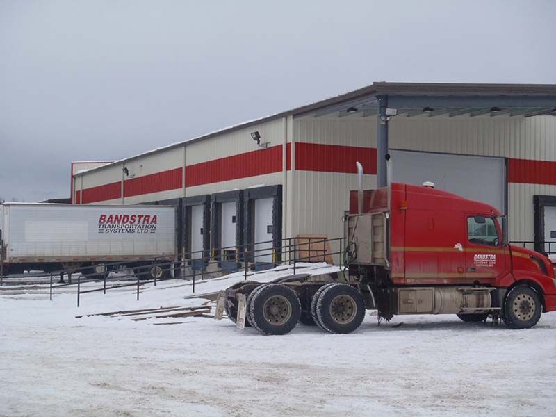 A red semi truck is parked in front of a building that says bandstra