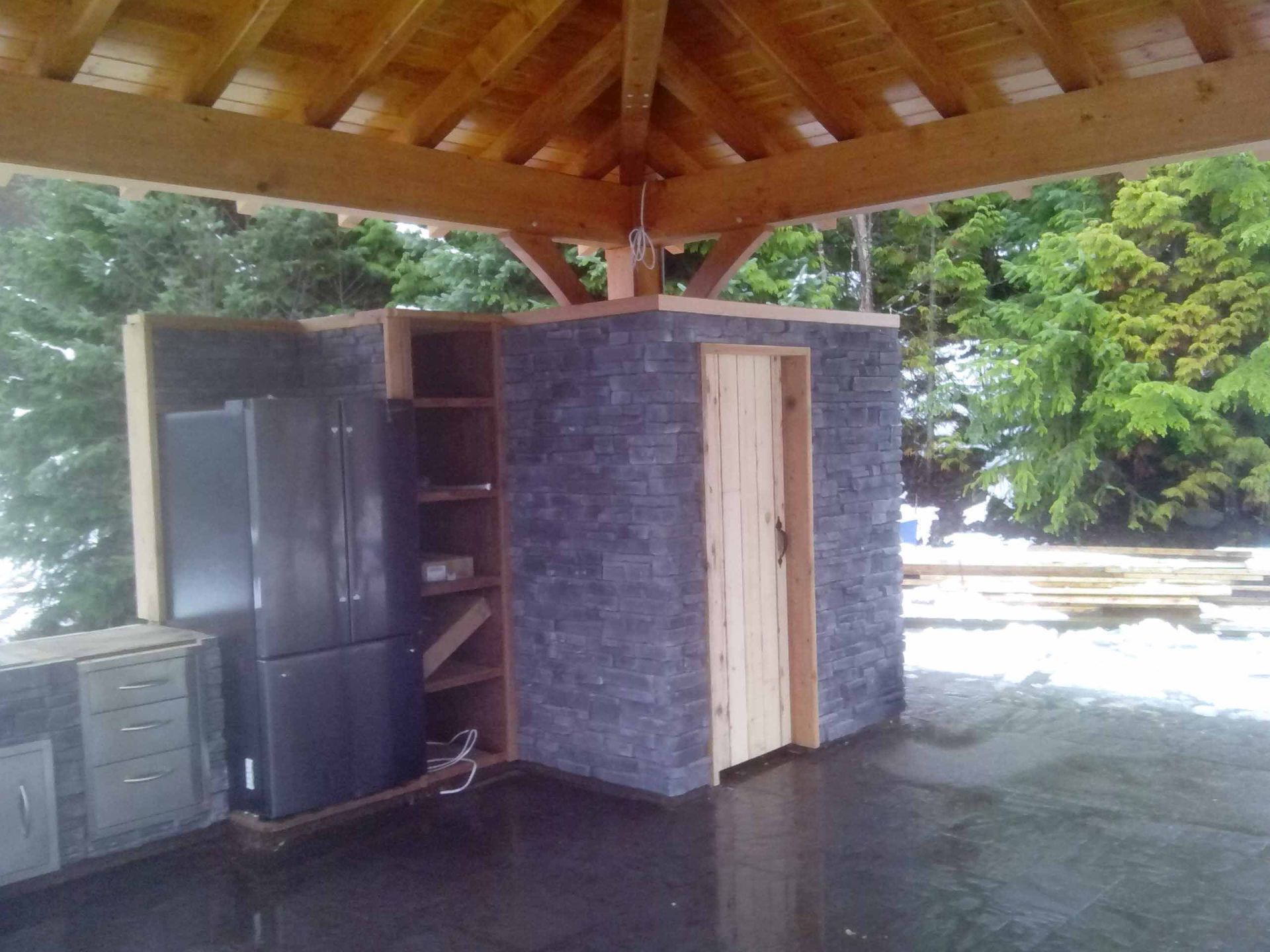 A room with a refrigerator and a door under a wooden roof