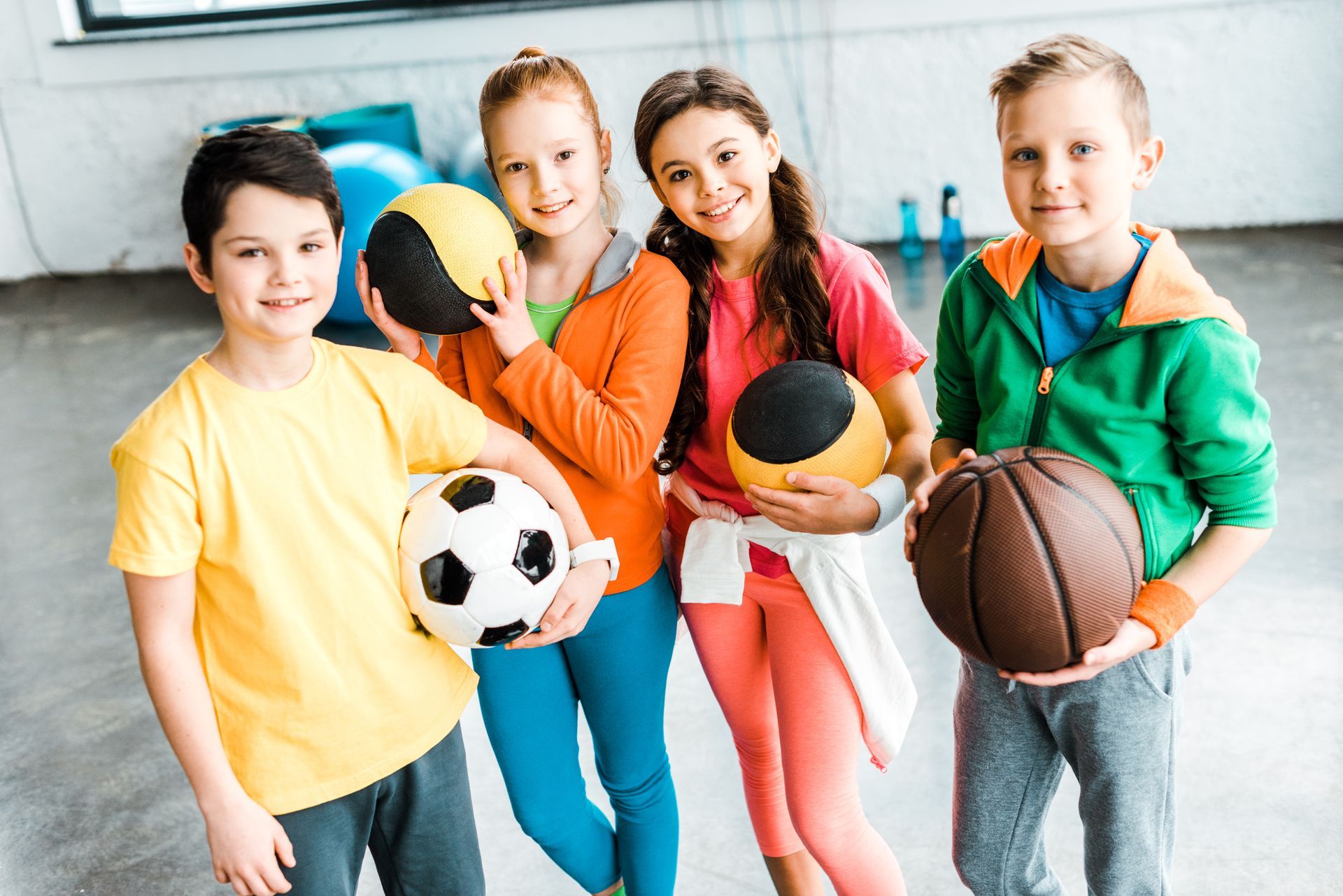 A group of children are holding basketballs and soccer balls.