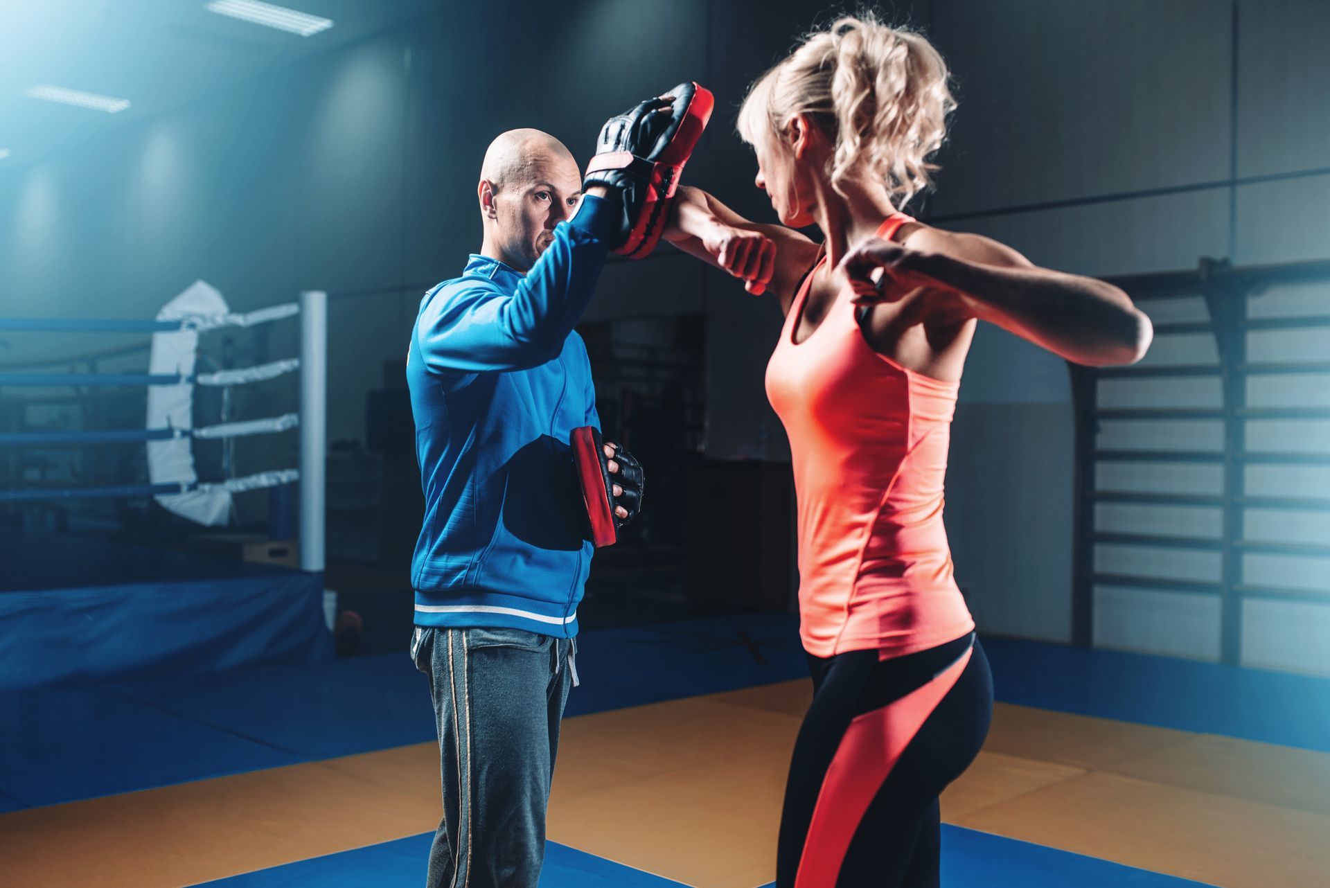 A man is teaching a woman how to box in a gym.