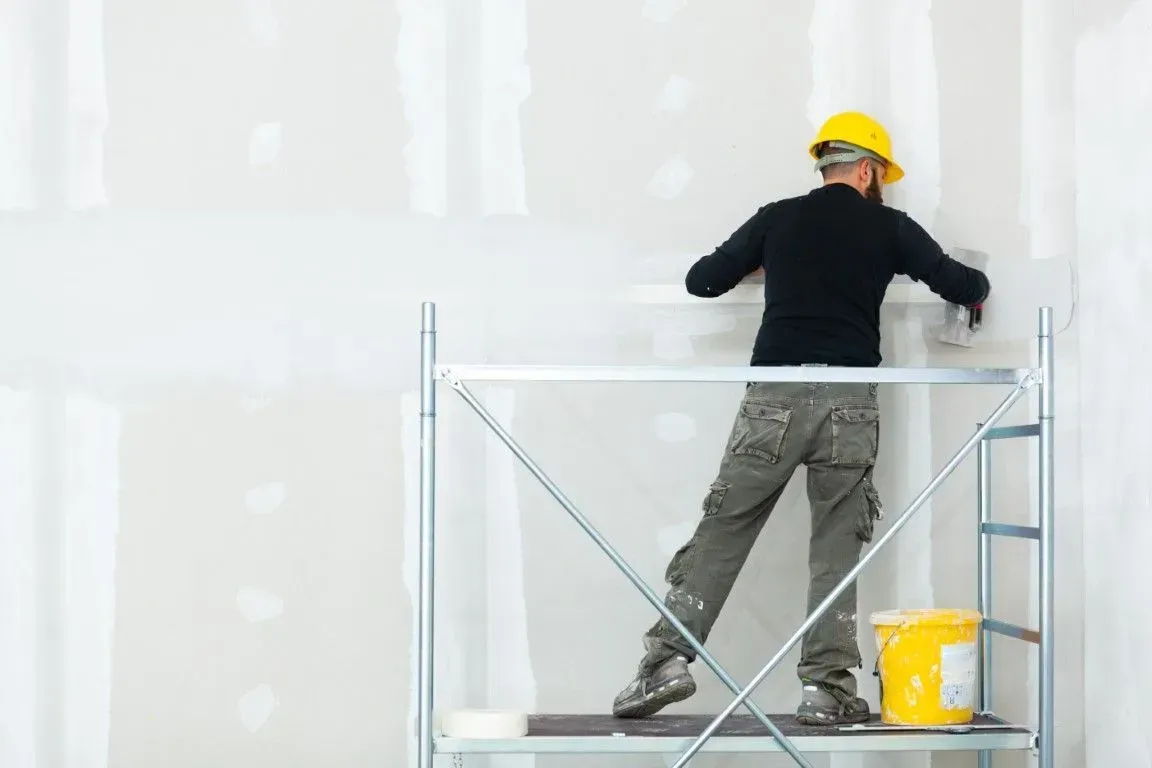 Construction worker plastering a drywall on scaffolding.