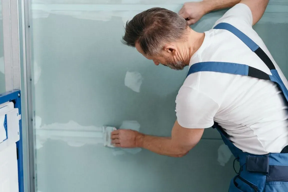 Worker applying joint compound to green drywall seams.