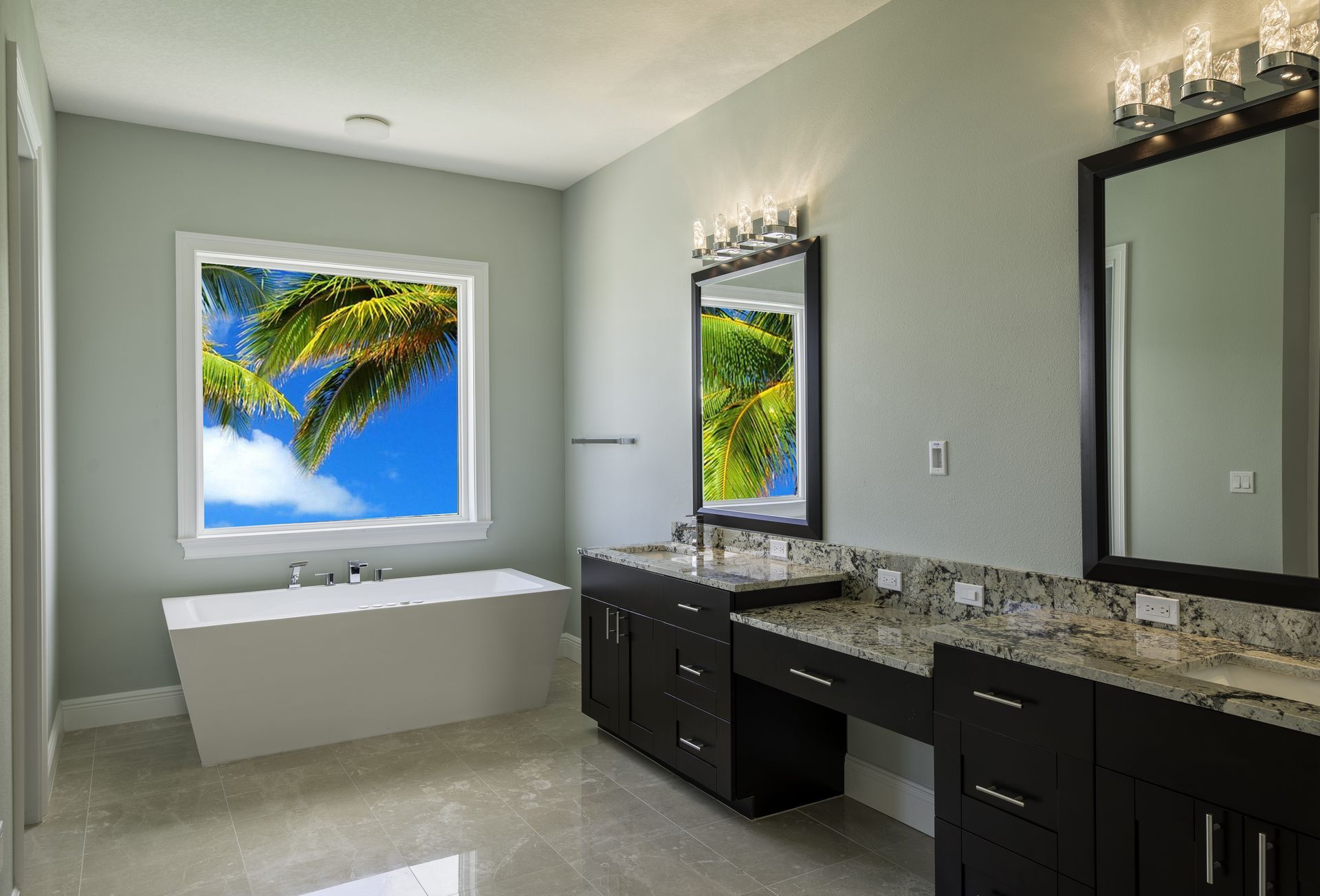 A modern bathroom with a white freestanding tub, a long dark vanity with granite countertops, and two framed mirrors.
