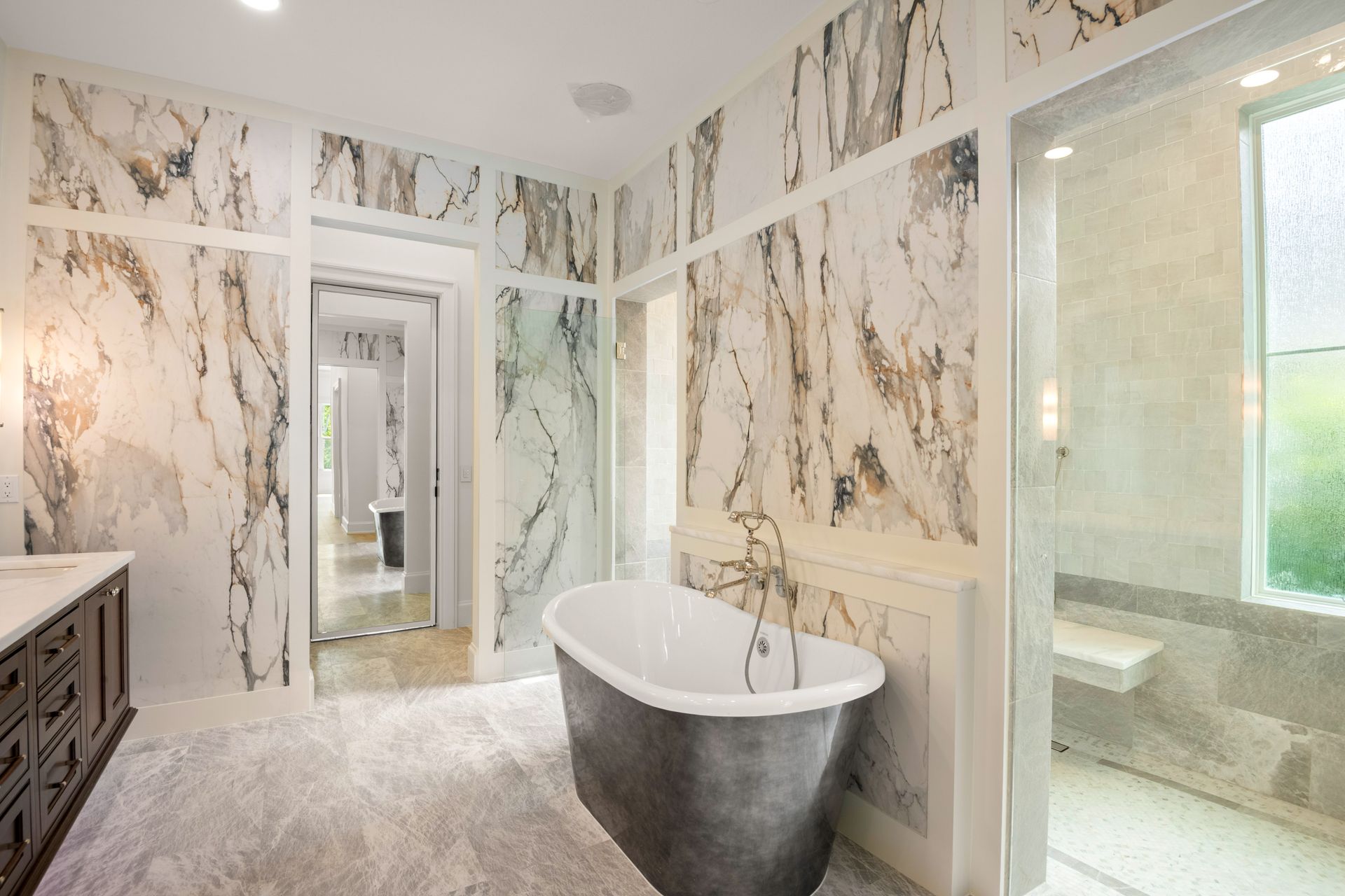 A luxurious bathroom featuring a freestanding silver tub, marble walls, and a glass-enclosed shower area.