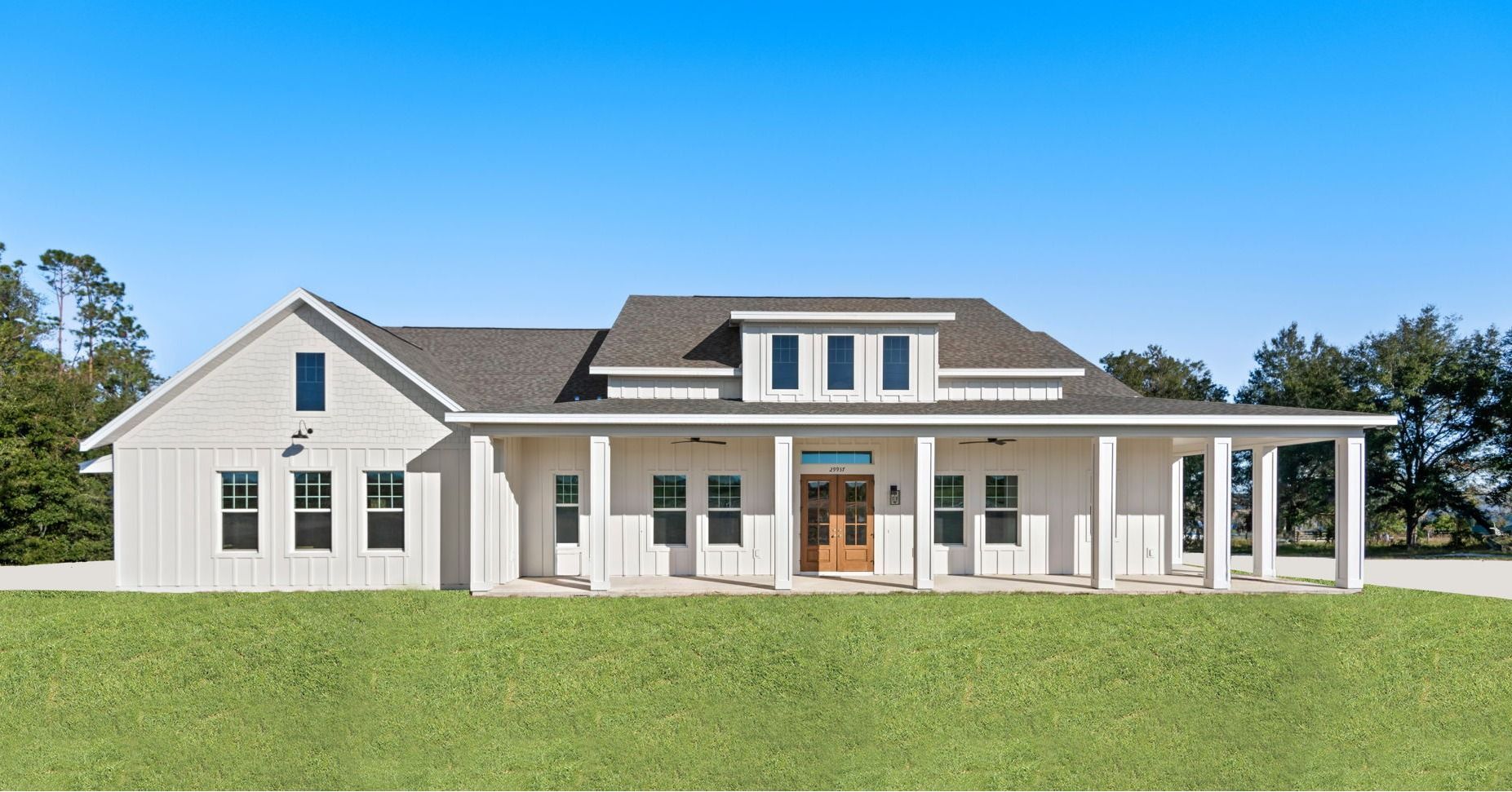 White farmhouse with long porch, windows, and brown door on a green lawn under a blue sky.