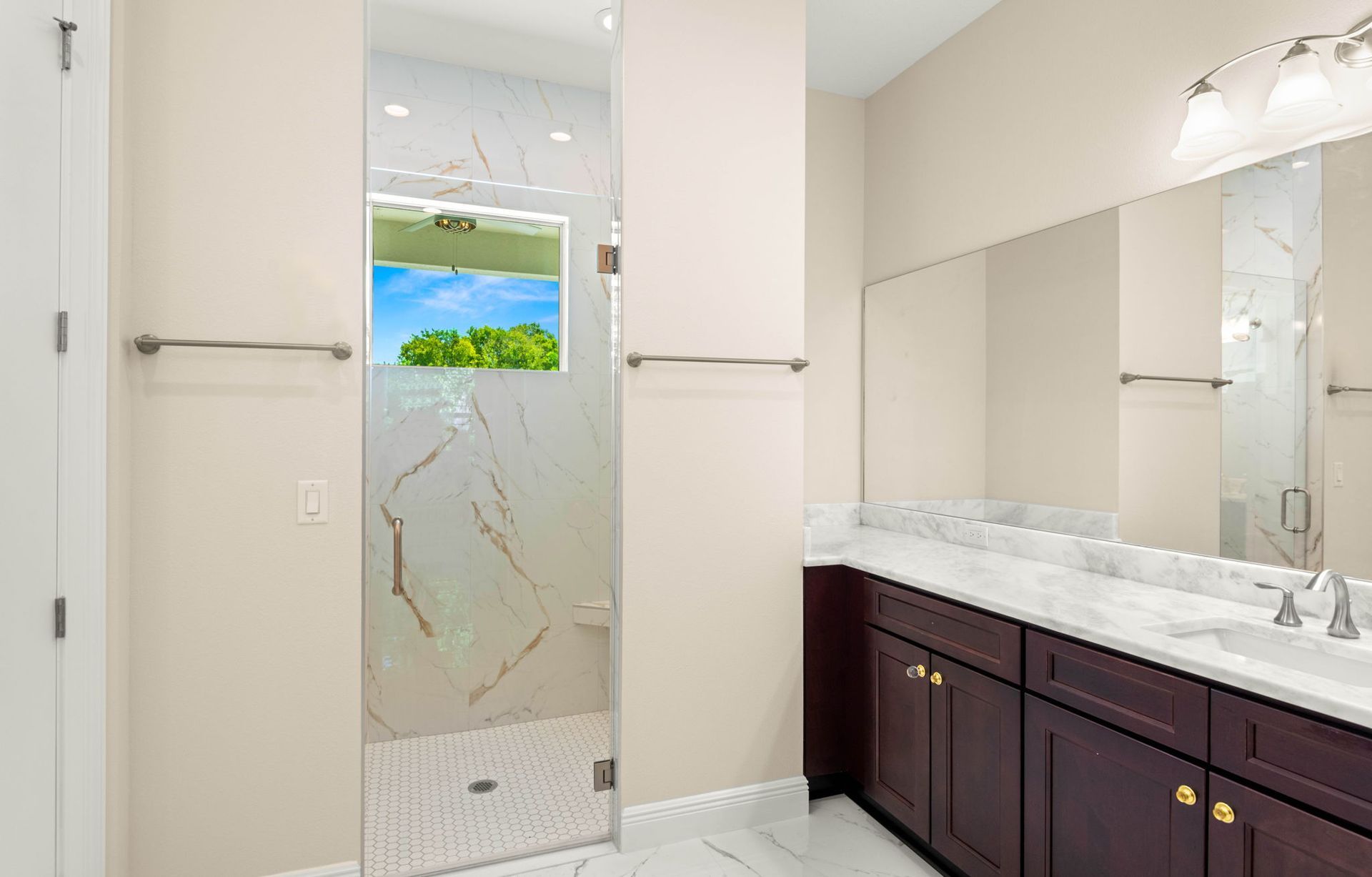 A modern bathroom with a glass-enclosed shower, marble-style tiling, and a dark brown vanity with a white countertop.