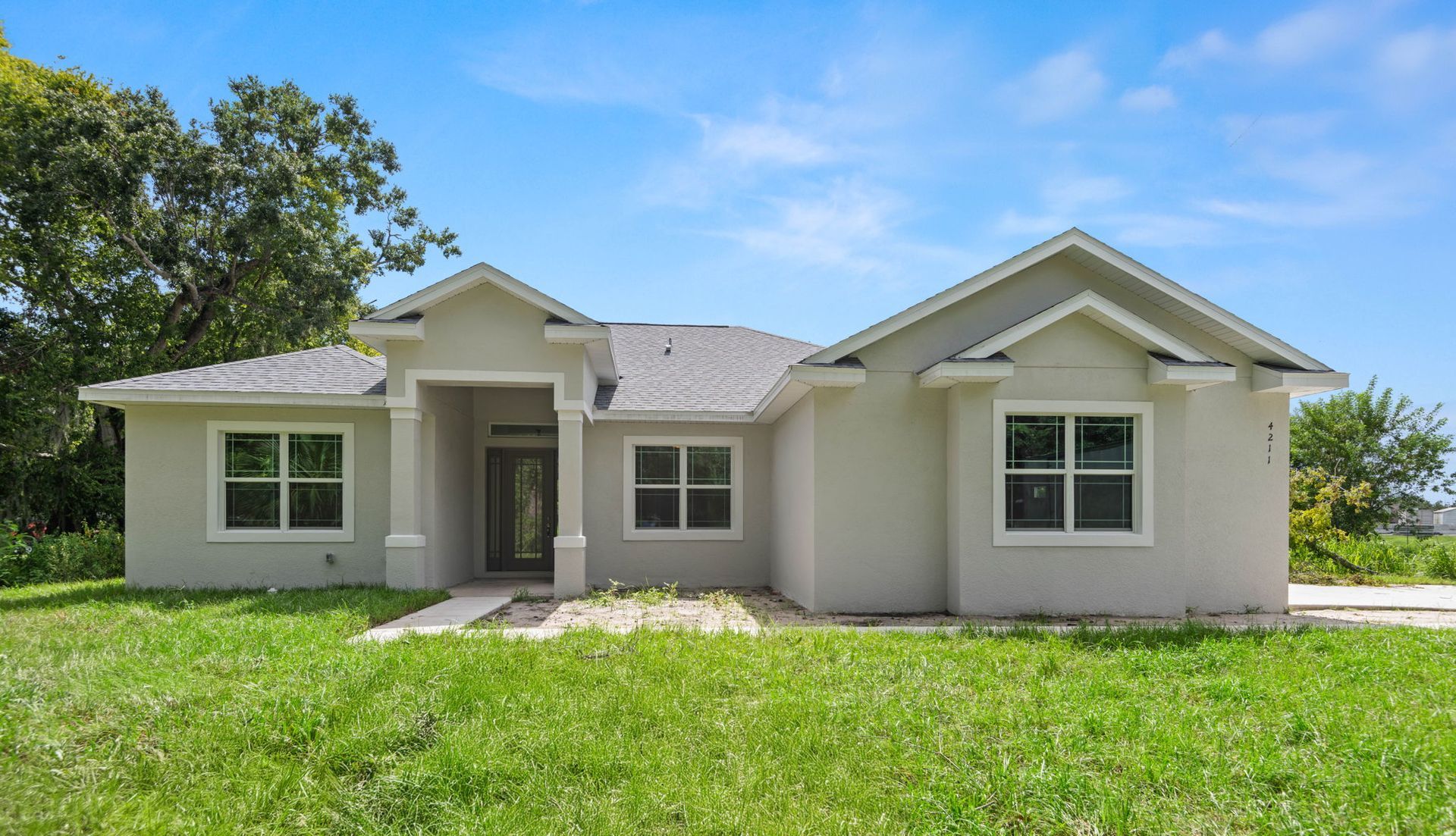 White farmhouse with a long porch, three dormers, and a green lawn under a colorful sunset.