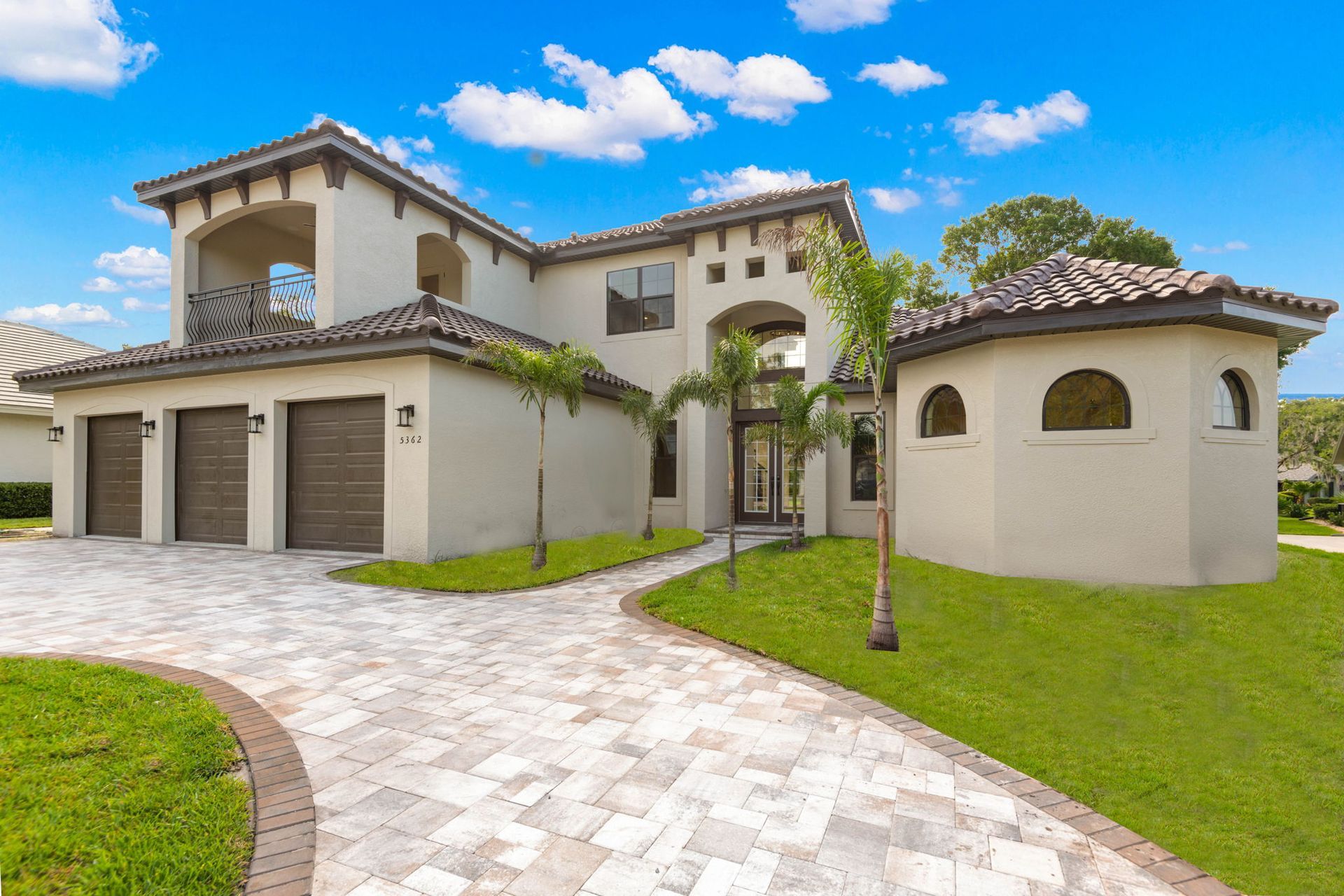 Mediterranean-style house with a brick driveway, garage, and a small tower under a blue sky.