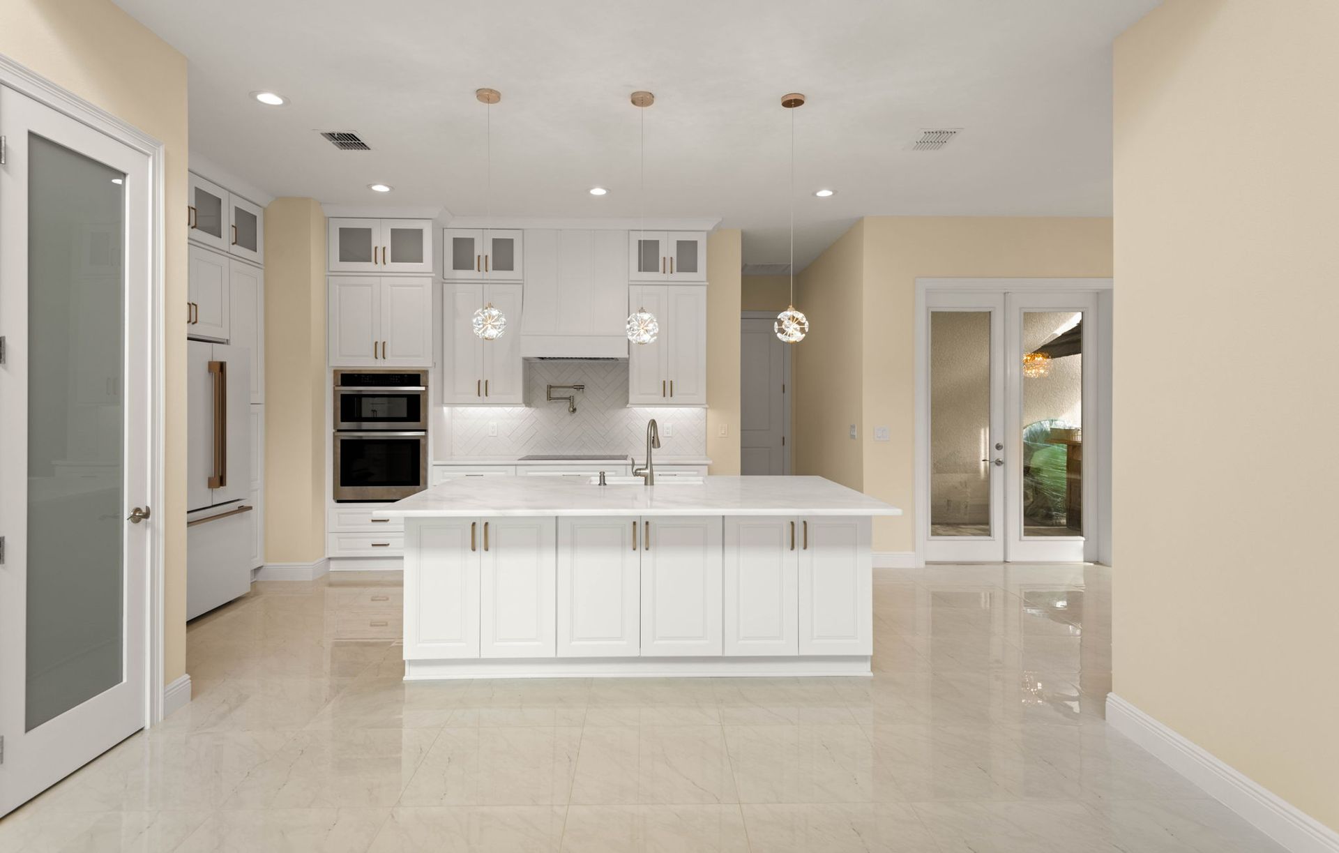 Bright, modern kitchen with white cabinets, island, and appliances. Tile floor, recessed lighting.