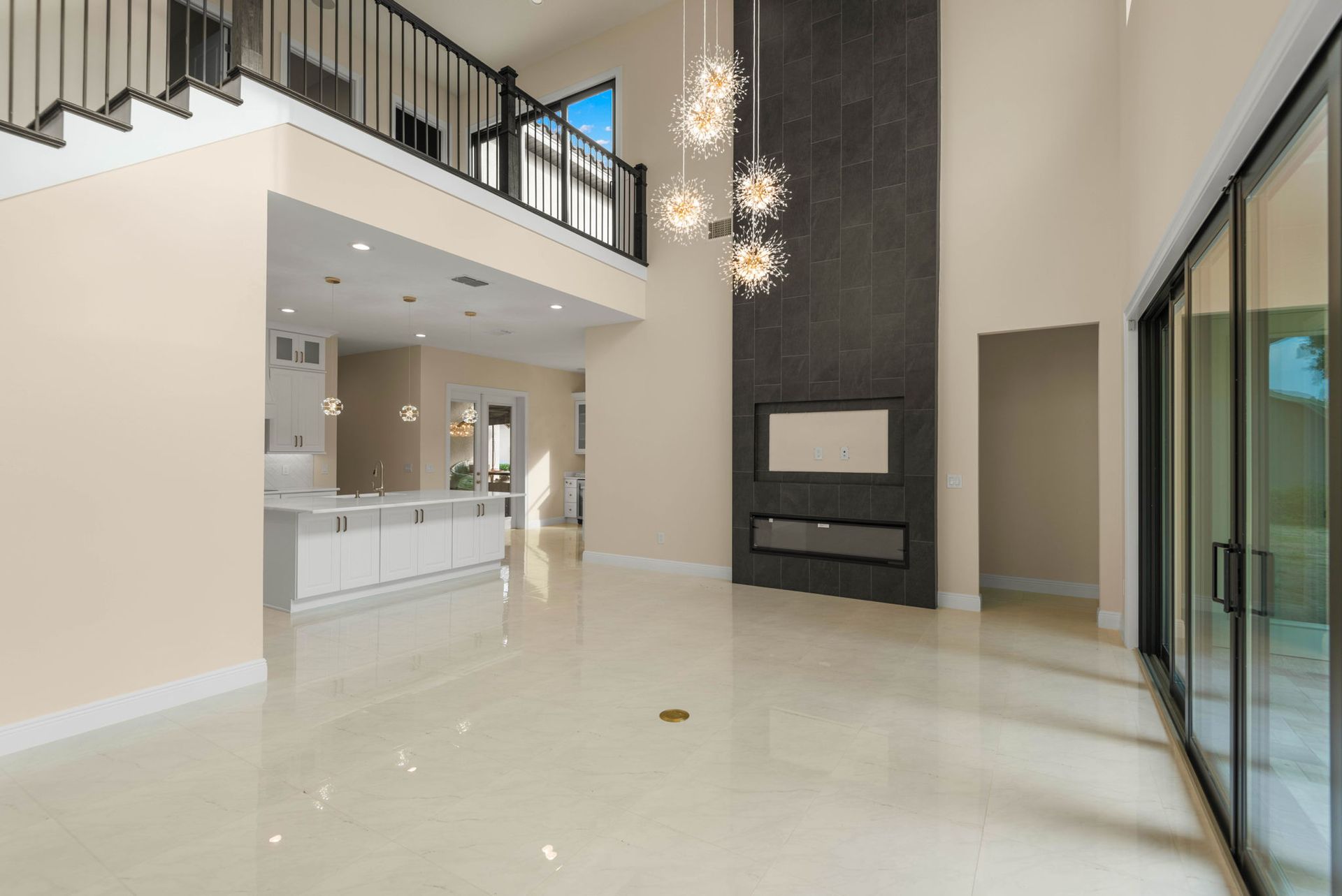 Spacious interior with fireplace, stairs, and sliding glass doors. Cream walls, light tile floor, and chandelier.