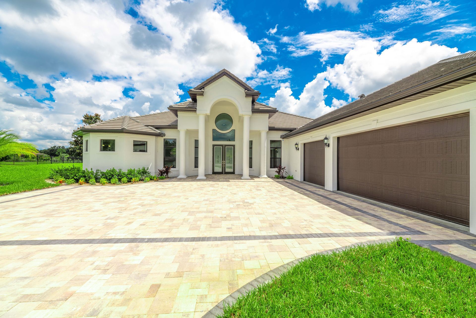 White mansion with columns, brown garage doors, and paved driveway on a sunny day.